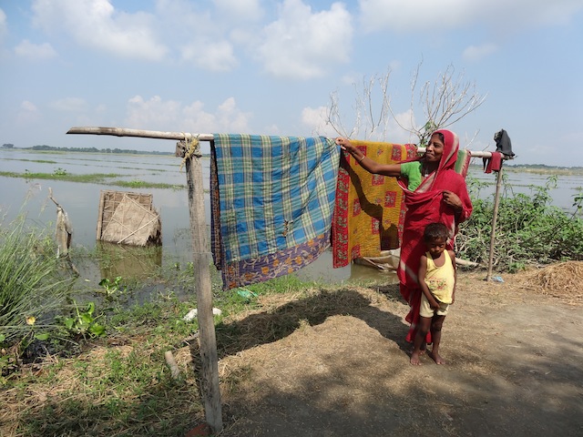 A woman dries blankets after her home went underwater for five days in one of the villages of the Morigaon district. The woven bamboo sheet beyond the clothesline used to be the walls of her family’s toilet. August rains inundated 141 villages in the district. Credit: Priyanka Borpujari/IPS