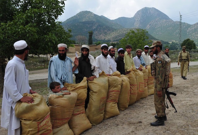 Army officers stand opposite displaced families as they collect their monthly allocation of food supplies in northern Pakistan. Credit: Ashfaq Yusufzai/IPS