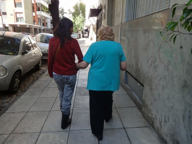 A caregiver assists her elderly employer on a residential street in Buenos Aires, Argentina. Credit: Fabiana Frayssinet/IPS
