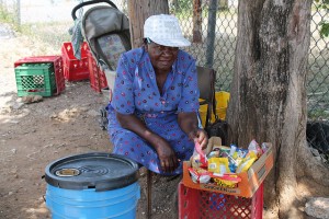 Seventy-year old Elise Young’s small box of mixed sweets and biscuits and the plastic bucket containing some ice and a handful of drinks is hardly enough to pay the 18-dollar electricity bill each month and buy food. Credit: Zadie Neufville/IPS