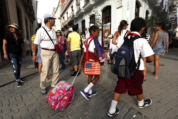 Two primary school students walk by a group of foreign tourists in a plaza in Old Havana. Credit: Jorge Luis Baños/IPS
