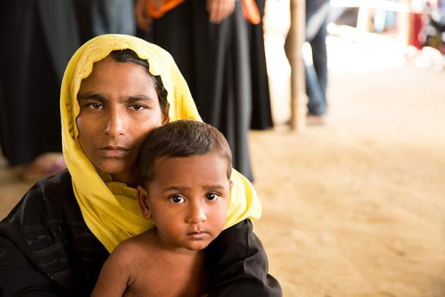 A woman waits to receive humanitarian aid with her child, having arrived in the Rohingya refugee settlement only moments before. Photo: Olivia Headon/UN Migration Agency (IOM) 2017