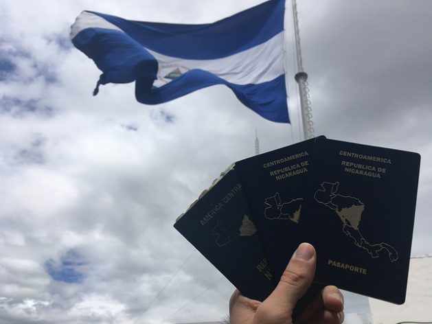 With a Nicaraguan flag in the background, passports from Nicaragua, with the silhouette of Central America on its cover, are held up. The country’s southern border with Costa Rica is closed by a "containment wall" policy that keeps out migrants travelling from South America towards the United States. Credit: José Adán Silva / IPS