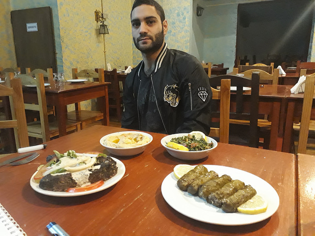 Fares al Badwan, who arrived in Argentina in 2011, when the bloody conflict in Syria was just beginning, shows some of the delicious Arab foods that are prepared in the family restaurant, including traditional hummus and tabouli. Credit: Daniel Gutman / IPS