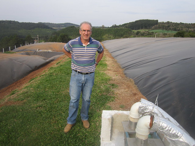 Pig farmer Anélio Thomazzoni stands next to the three biodigesters with which he currently produces biogas for the generation of 280,000 kilowatt/hours on his farm in the small municipality of Vargeão, in southern Brazil. Part of the biofuel will be purified to transform it into biomethane, while 6,000 square metres of solar panels are installed to generate 130,000 kilowatts/hour. Credit: Mario Osava/IPS