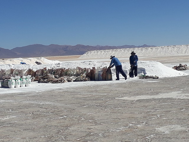 Two men from indigenous communities near Salinas Grandes pick up bags of salt harvested by members of the local cooperative. Villages around Salinas Grandes have blocked attempts to mine lithium in the area. Credit: Daniel Gutman/IPS