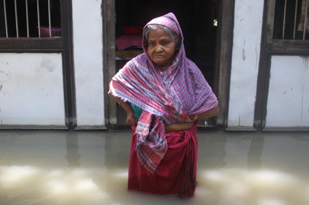 Manju Begum, 85, stands in front of her flooded house in Medeni Mandal in Munshiganj District, central Bangladesh. She says she has not received any assistance from local officials since her home was flooded more than a week ago. With nearly 5.5 million people people across Bangladesh affected by severe flooding, humanitarian experts are concerned that millions of people, already badly impacted by COVID-19, will be pushed further into poverty. Credit: Farid Ahmed/IPS