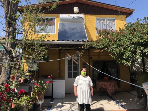 Schoolteacher Marta Pérez stands in front of her house near the solar thermo panel that has allowed her and her family to enjoy hot water again, because the high cost of electricity made it unaffordable in the past. There are a total of 70 beneficiaries of the solar water heater project in the town of Renca, to the north of Santiago, Chile. CREDIT: Orlando Milesi/IPS