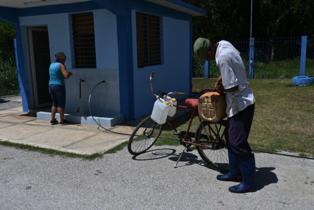 Two people collect drinking water in plastic containers at the intake of the pumping station of the desalination plant located in Las Mangas, Granma province, Cuba. Credit: Jorge Luis Baños / IPS