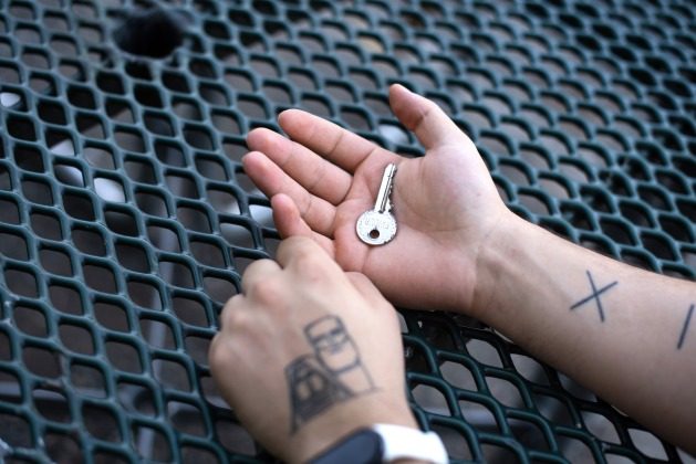 Hayk Harutyunyan, a 22-year-old displaced photographer from Nagorno-Karabakh, holds the key to his house in Nagorno-Karabakh. A tattoo of the monument “We are our mountains,” a symbol of Nagorno-Karabakh, can be seen on his arm. Credit: Gayane Yenokian/IPS.