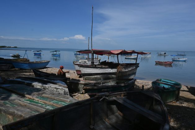 A fisherman sits next to several boats at the GeoCuba Local Interest Fishing Port in the bay of Manzanillo, in the eastern Cuban province of Granma. Credit: Jorge Luis Baños / IPS