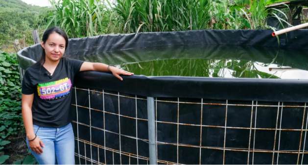 Merlyn Sandoval next to the rainwater collection tank built on the small plot where she lives, in the village of San Jose Las Pilas, in eastern Guatemala. She and her family participate in a program to alleviate the effects of the drought in the Central American Dry Corridor. Credit: Edgardo Ayala / IPS