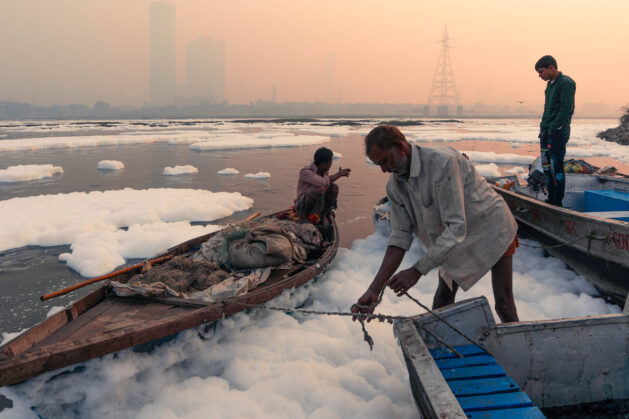 Fishermen on the banks of the river Yamuna, surrounded by clouds of toxic foam on the water surface. Credit: Raunaq Singh Chopra / Climate Visuals