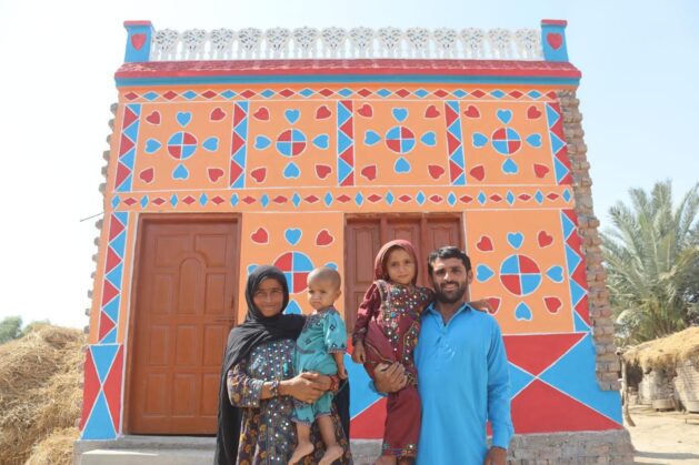 A family poses in front of their home rebuilt as part of the Sindh People’s Housing for Flood Affectees (SPHF). At COP30 the project was showcased for its significant successes in empowering women in the rehousing the families of the devastating 2022 floods. Credit: SPHF