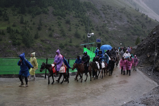 Pilgrims, accompanied by pony operators and porters, continue their journey along the Baltal route during rain on the annual Amarnath Yatra in Jammu and Kashmir in July 2026. Credit: Umar Manzoor Shah/IPS