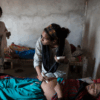 A community health worker examines a pregnant woman inside her home while family members look on, highlighting the growing challenges mothers face as extreme heat and climate-related pressures strain access to healthcare in vulnerable communities. Credit: Wellcome