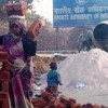 A woman labourer balances a pile of bricks on her head outside the main Commonwealth Games stadium while her child plays. Credit: Ranjit Devraj/IPS