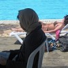 A woman wearing hijab sits beside another in a bikini.  Credit: Mona Alami/IPS