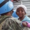 A UN peacekeeper holds a child as her mother is helped down from a relocation truck in Port-au-Prince, Haiti. Credit: UN Photo/Logan Abassi