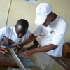 Jean Ronel Noël of ENERSA helps a Senegalese technician solder a solar panel. Credit: ENERSA