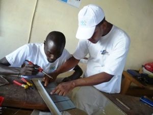 Jean Ronel Noël of ENERSA helps a Senegalese technician solder a solar panel. Credit: ENERSA